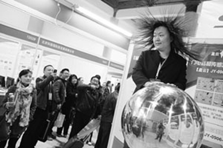 2012北京教育装备展上,一名老师将手放在静电演示装备上,头发立刻“爆炸”